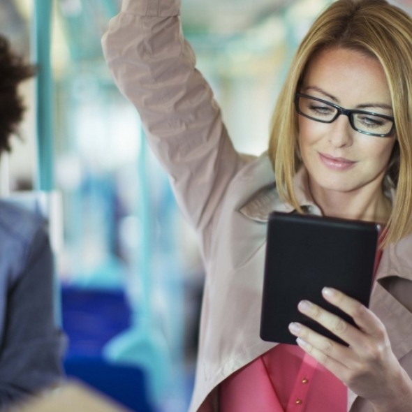 Woman wearing glasses on train reading tablet 