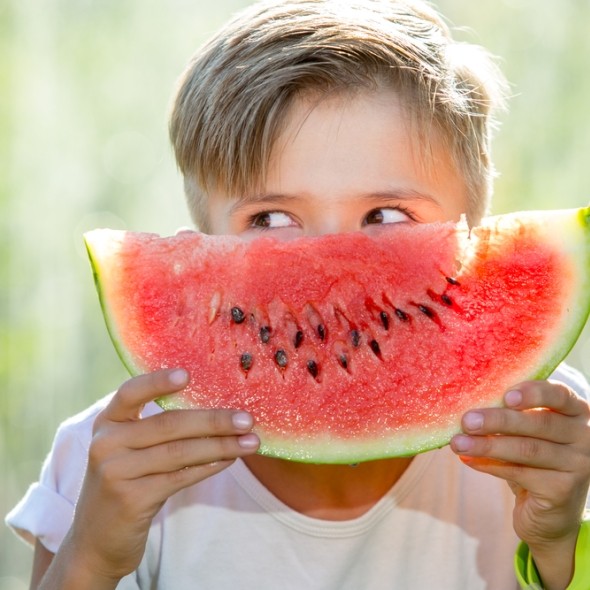 young boy hold a slice of watermelon in front of face