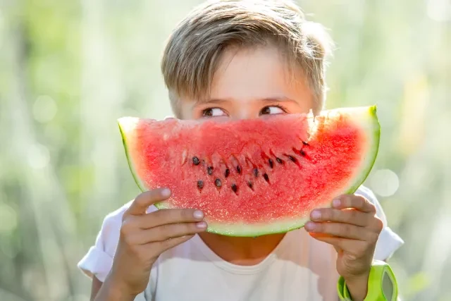 young boy hold a slice of watermelon in front of face